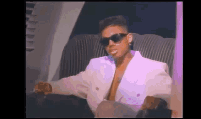 a man wearing sunglasses and a white jacket is sitting in a chair .