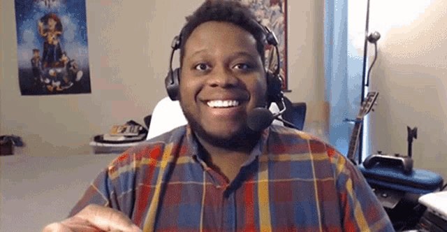 a man wearing headphones and a plaid shirt is smiling in a room .