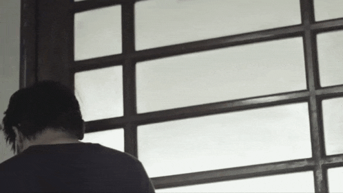 a man in a black shirt is standing in front of a window looking out .