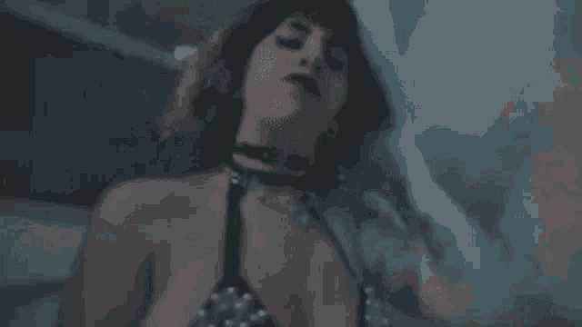 a woman in a black bra and choker is laying on a bed in the dark .