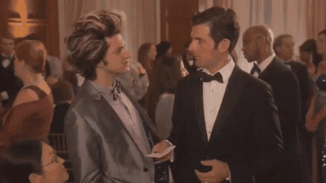 two men in tuxedos are dancing together in a room with a crowd of people .