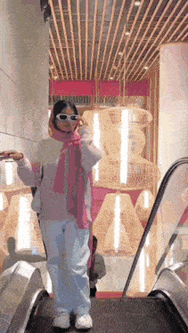 a woman wearing sunglasses and a pink scarf is riding an escalator in a store .