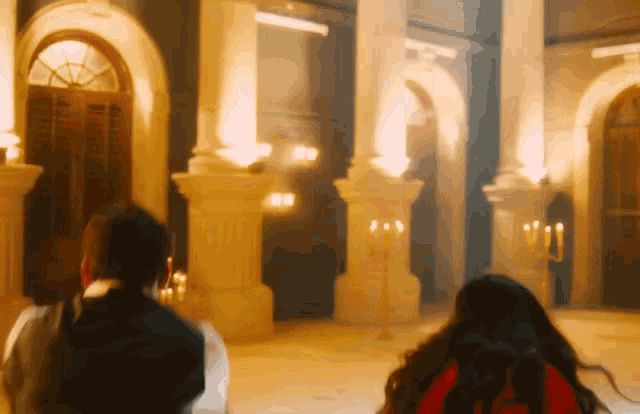 a man and a woman are standing in a large room with columns and candles .
