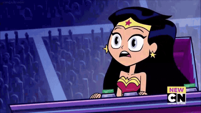 wonder woman is sitting at a desk in front of a crowd of people .