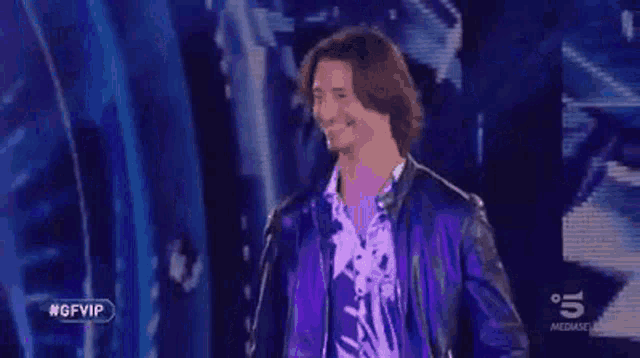 a man in a leather jacket is standing on a stage in front of a blue background .
