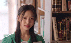 a woman in a green dress is sitting in a library reading a book .