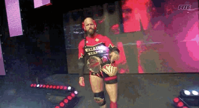 a wrestler wearing a red shirt that says walking weapon is walking on the stage .