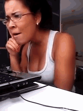 a woman wearing glasses and a white tank top is sitting in front of a laptop computer