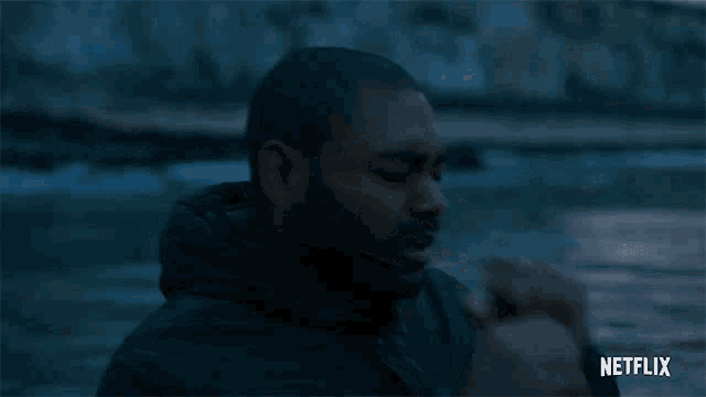 a man with a beard is standing in front of a body of water in a netflix trailer .