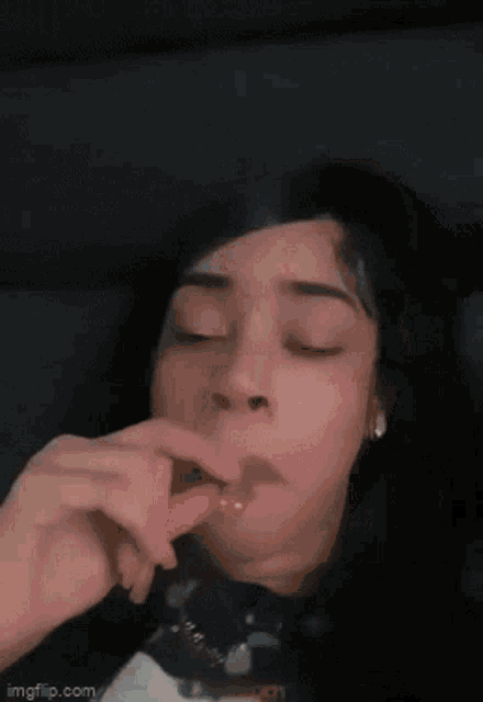 a woman is smoking a cigarette with her eyes closed and smoke is coming out of her mouth .