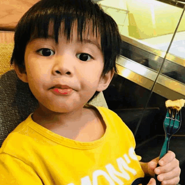 a young boy wearing a yellow shirt that says " ok " holds a fork