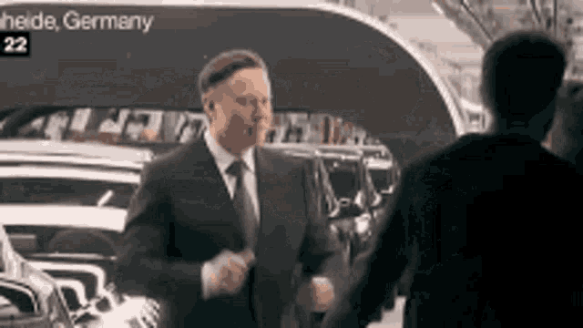a man in a suit and tie is shaking hands with another man in front of a sign that says heide germany
