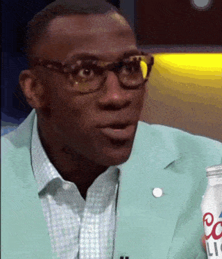 a man wearing glasses and a green jacket is holding a bottle of liqour