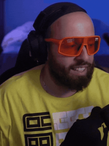 a bald man with a beard wearing orange sunglasses and a yellow shirt