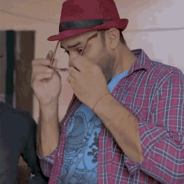 a man wearing a plaid shirt and a red hat holds a pair of glasses
