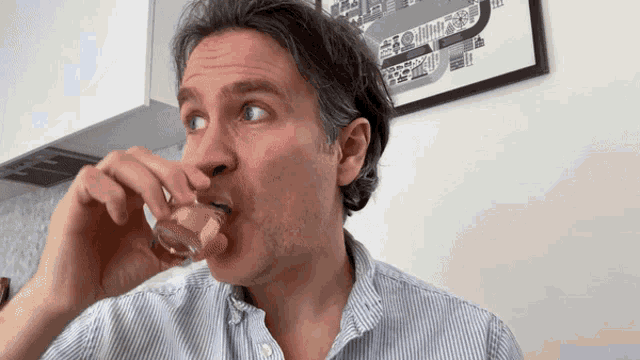 a man in a striped shirt drinks from a glass in front of a framed picture