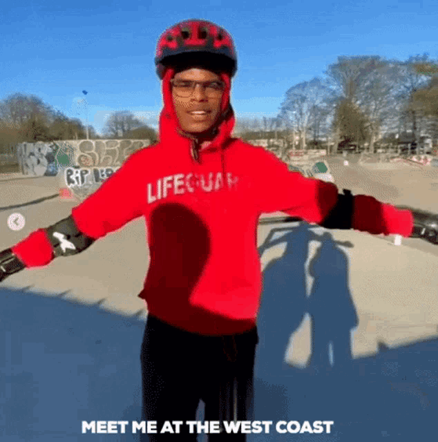 a man wearing a red lifeguard hoodie is standing in a skate park with his arms outstretched