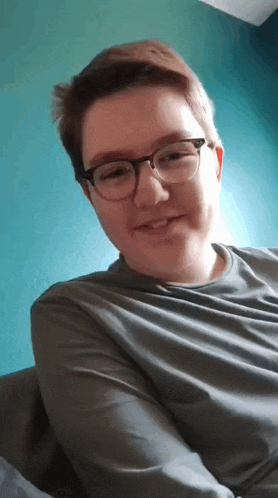 a man wearing glasses and a grey shirt is smiling