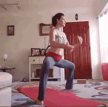a woman is squatting on a red yoga mat in a living room
