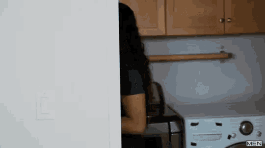 a woman is standing in a laundry room next to a washer and dryer and the word men is on the wall behind her