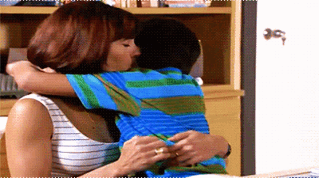 a woman is hugging a boy in a blue and green shirt