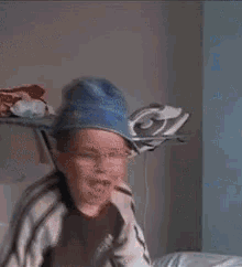 a young boy wearing a blue hat and glasses is sitting on a bed with his mouth open
