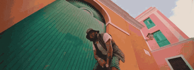 a man in a hat sits in front of a pink building