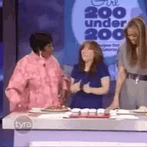a group of women are standing around a table with plates of food in front of a sign that says 200 under 200 .