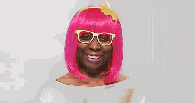 a woman wearing a pink wig and glasses smiles