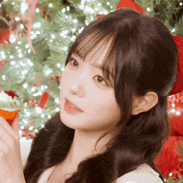 a girl is holding a cupcake with a green frosting in front of a christmas tree