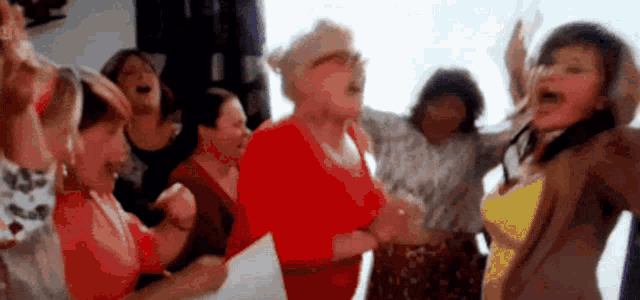 a group of women are singing together in a room with their arms in the air .