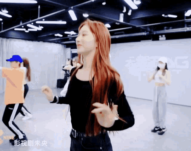 a girl with long red hair is dancing in a room with chinese writing on the wall behind her