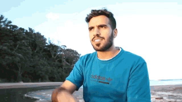 a man wearing a blue adidas t-shirt stands on a beach