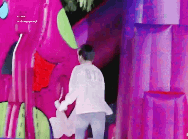 a man in a bts shirt is standing in front of a pink inflatable dinosaur .