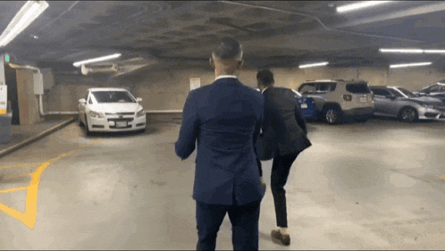 two men standing in a parking garage looking at a car