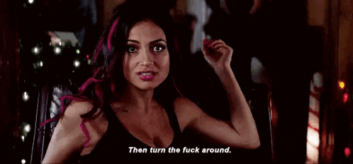 a woman with pink hair is sitting in a chair holding a pink object and says `` then turn the fuck around . ''