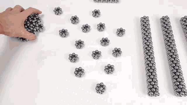 a person is playing with a bunch of metal balls on a white surface