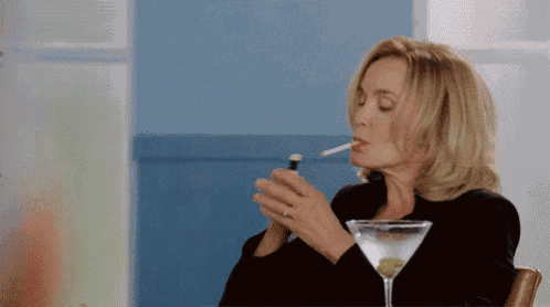 a woman is smoking a cigarette while sitting at a table with a martini glass