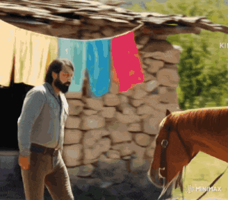 a man with a beard is standing next to a horse in front of a stone wall .