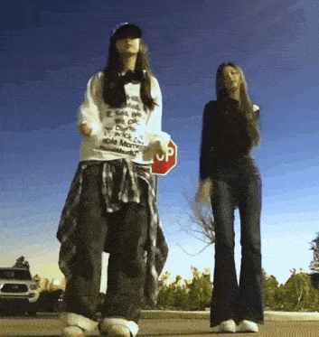 two women are dancing in front of a red stop sign