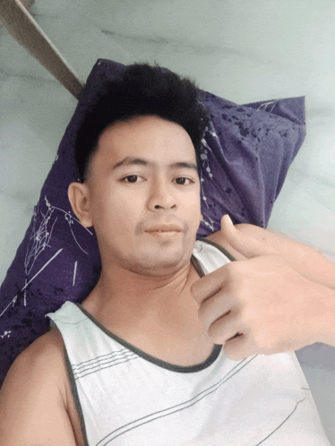 a man in a white tank top laying on a purple pillow giving a thumbs up