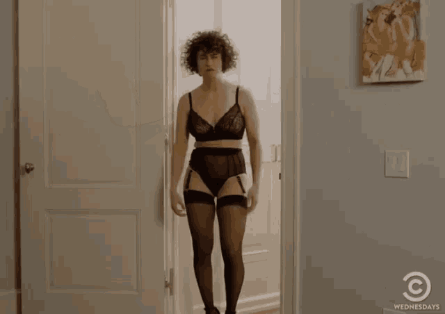 a woman in lingerie is standing in a doorway with a wednesdays logo in the corner .