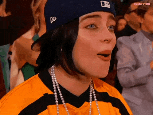 billie eilish is wearing a baseball cap and a yellow and black striped shirt .