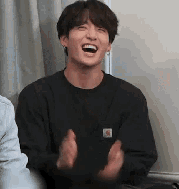 a close up of a person wearing a black sweater laughing and clapping .