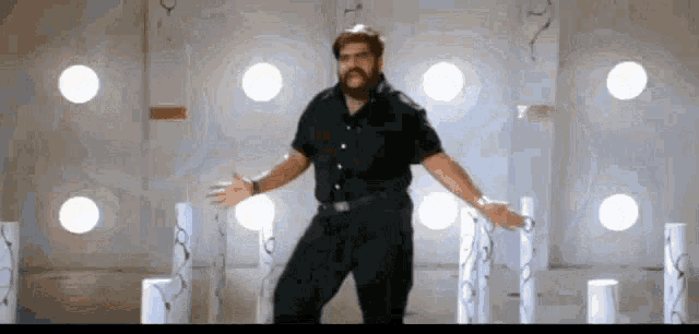 a man in a black shirt and black pants is dancing in a room with white pillars .