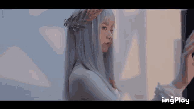 a woman with long white hair and a wreath on her head is standing in front of a window .