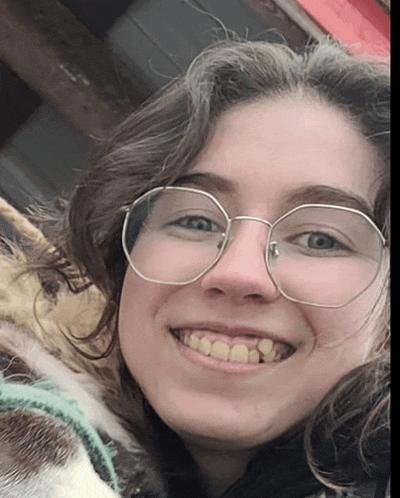 a woman wearing glasses is smiling with a dog behind her