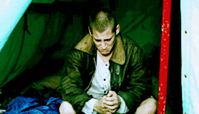 a man is sitting in a tent with his hands folded