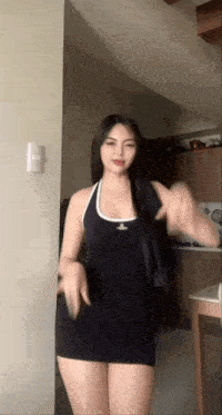 a woman in a black dress is standing in a kitchen .