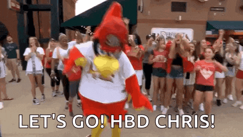 a mascot is standing in front of a crowd of people and says `` let 's go ! hbd chris ! ''